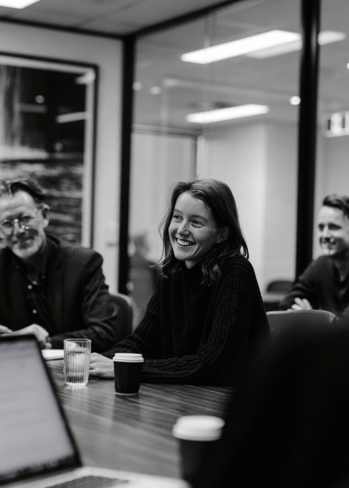 Three colleagues around a boardroom table, one laughing mid-conversation